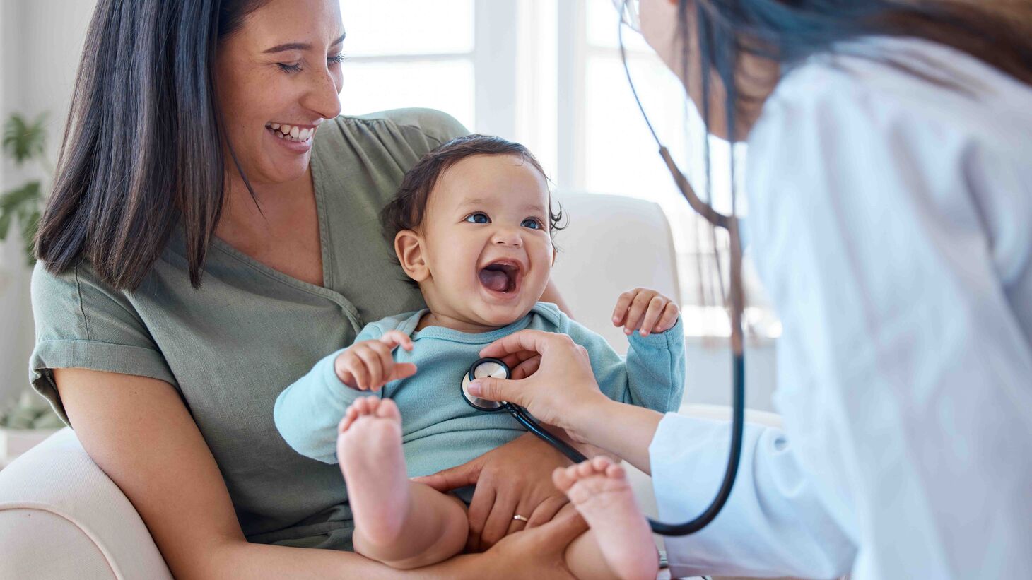 woman holding smiling baby, doctor using stethoscope on baby