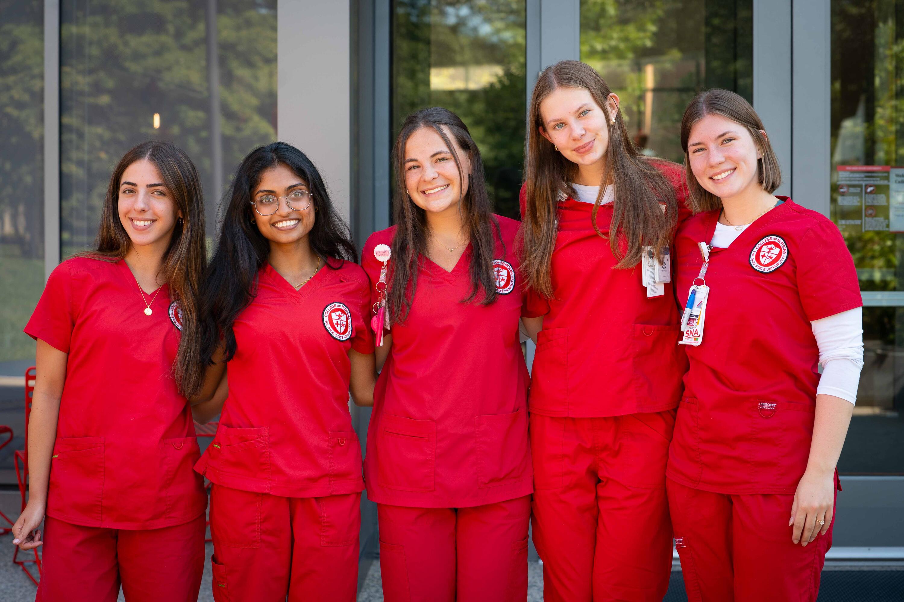nursing students in red scrubs pose in front of Heminger Hall