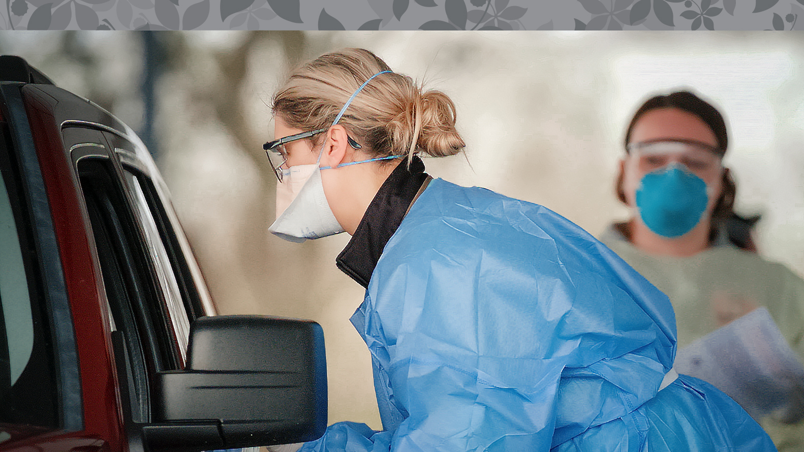 nurse wearing mask speaking to someone in car at a drive through testing station