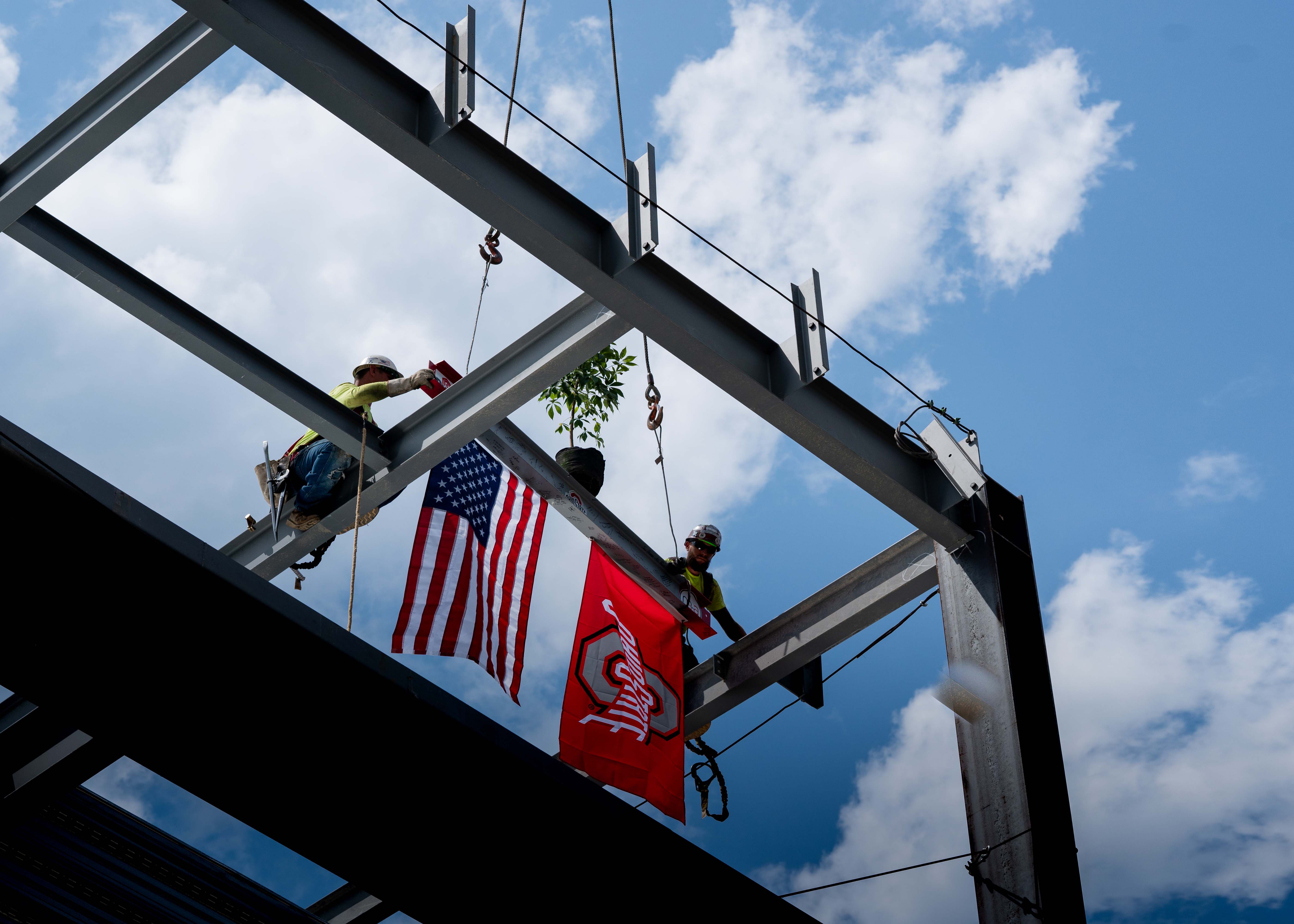 final beam being placed on top of building with American and Ohio State flags and buckeye tree on top