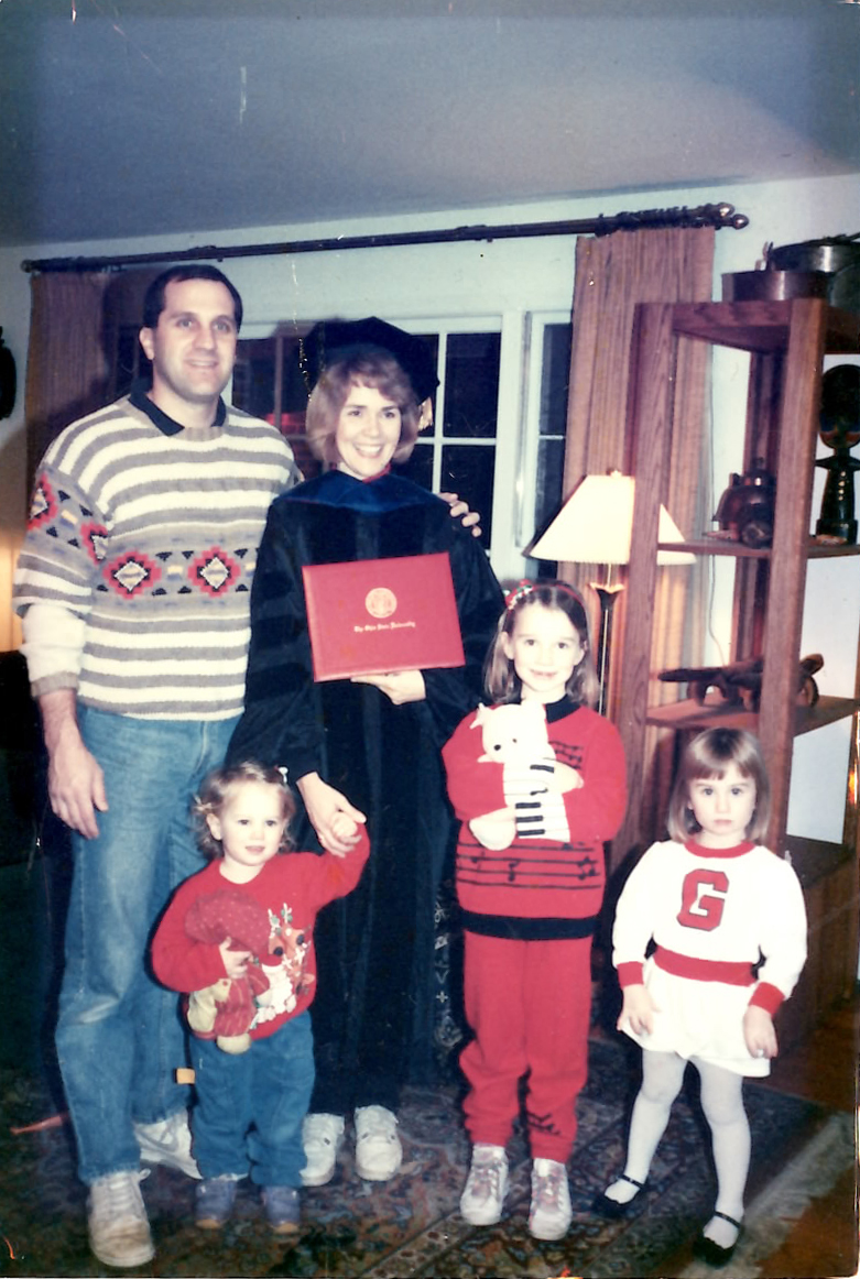 Margaret Graham in graduation regalia holding diploma and posing with her husband and children
