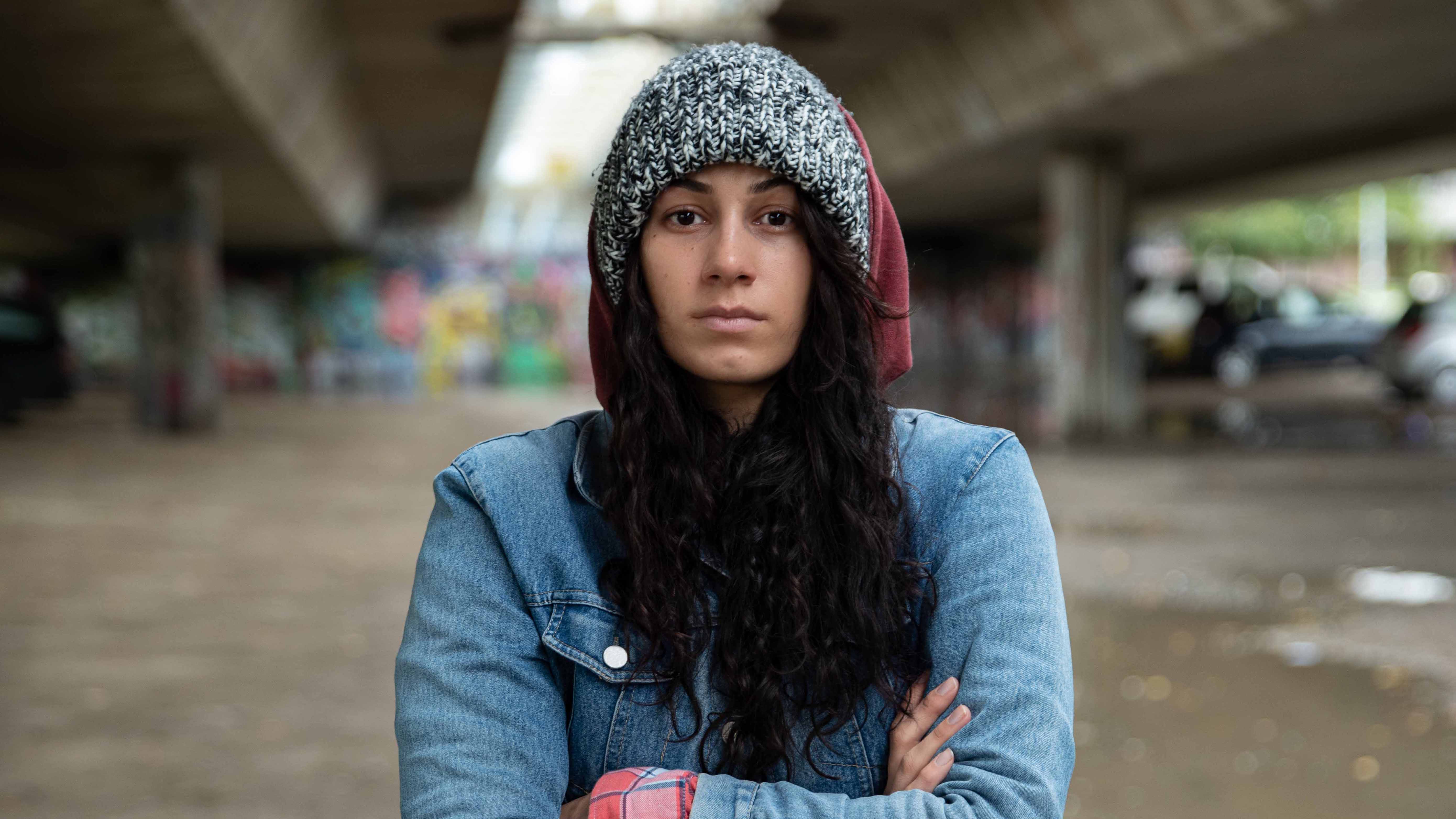 young woman on street with hood up and arms crossed