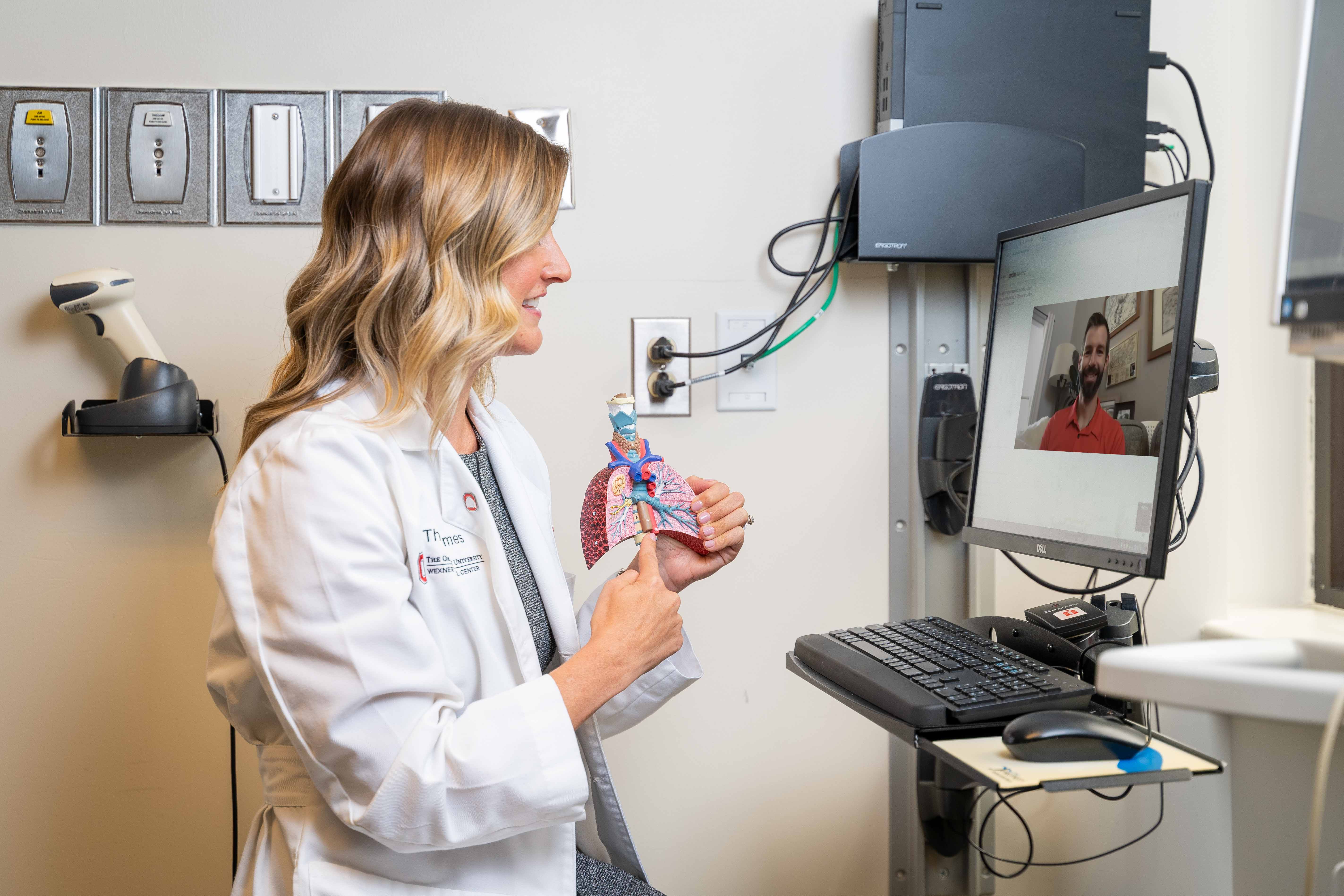Cassie Walker holding model lungs while talking to patient via telehealth technology
