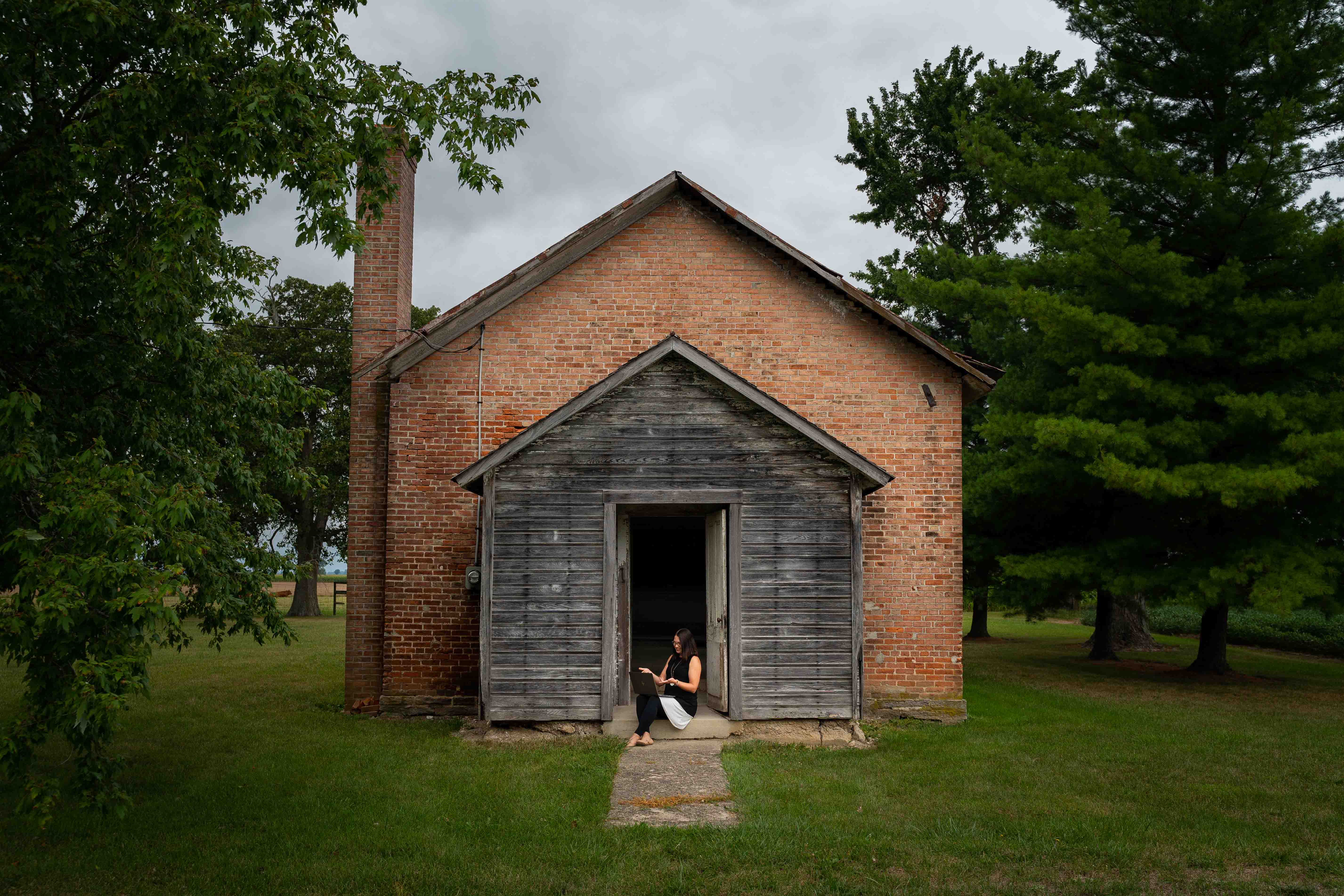 Christa Newtz outside sitting on the step of an old one-room schoolhouse