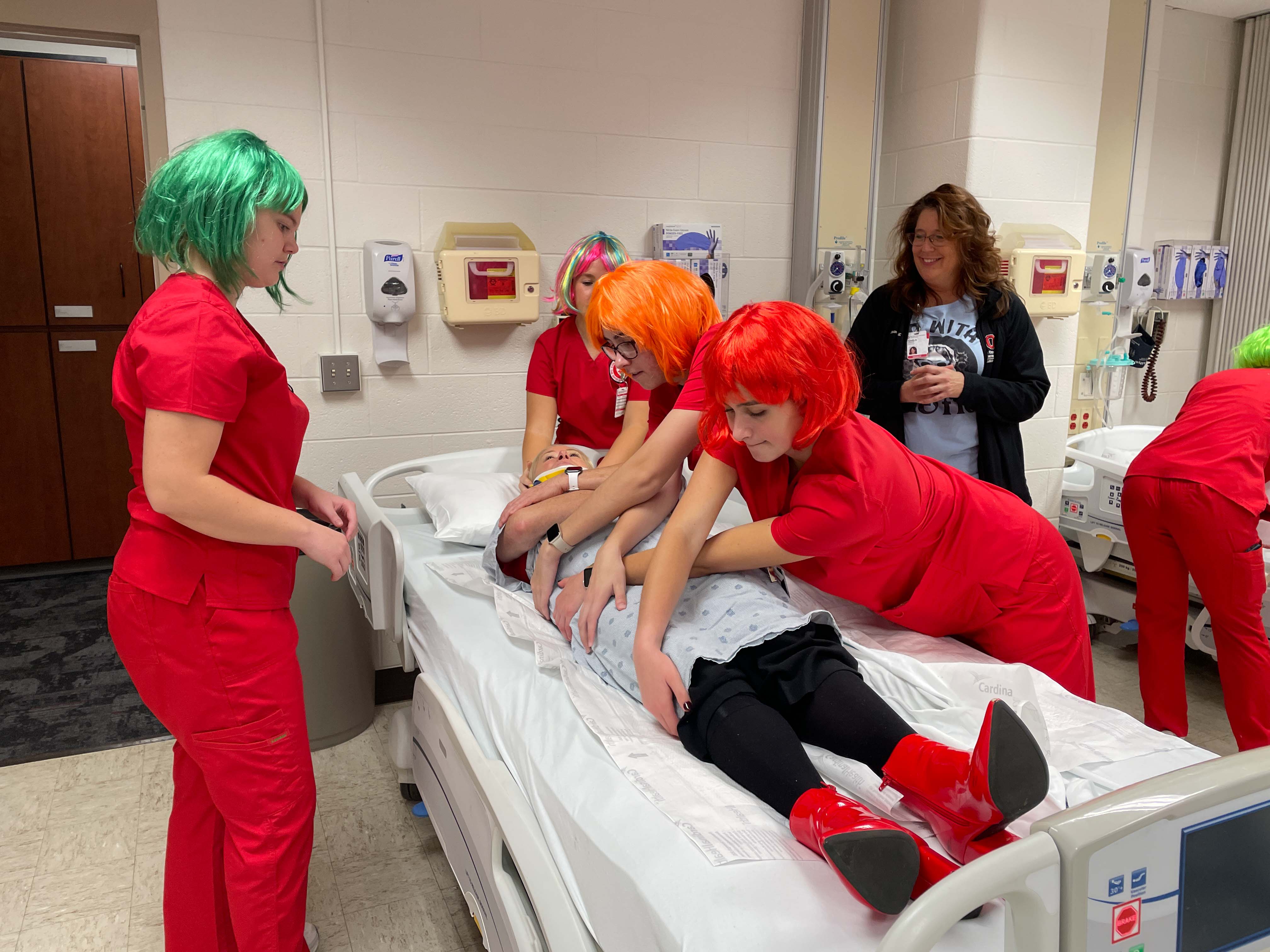 A clinical group practices their log-rolling skills on faculty volunteer, Janine Overcash, who role plays a patient with a neck injury.