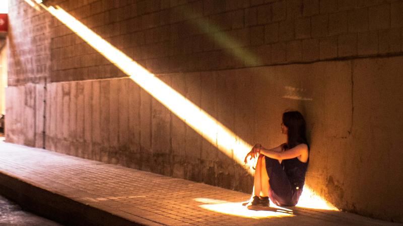 Adolescent girl sitting under overpass looking toward to the light