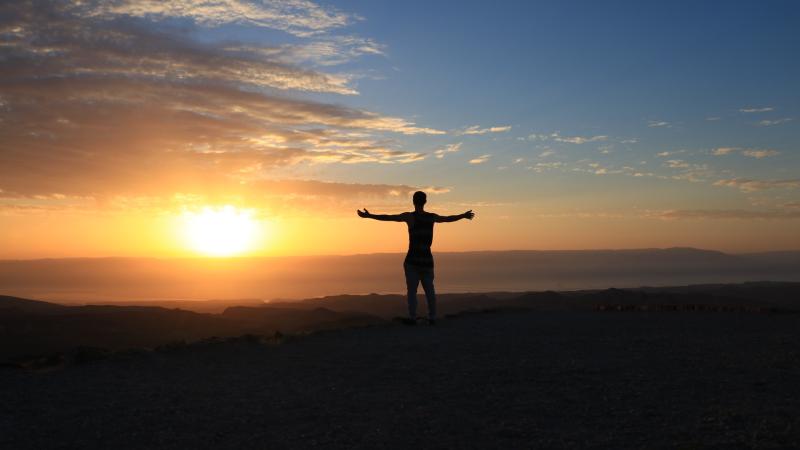 silhouette of man with arms outstretched in front of a sunset