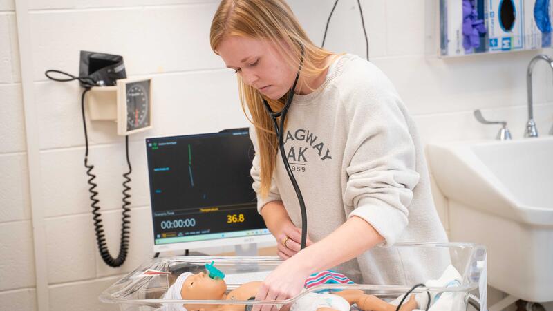 nursing student uses stethoscope on baby mannequin in lab