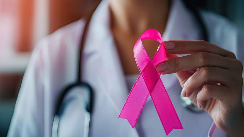 physician in white coat holding pink breast cancer ribbon