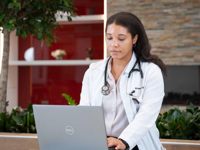 student in white coat works on laptop