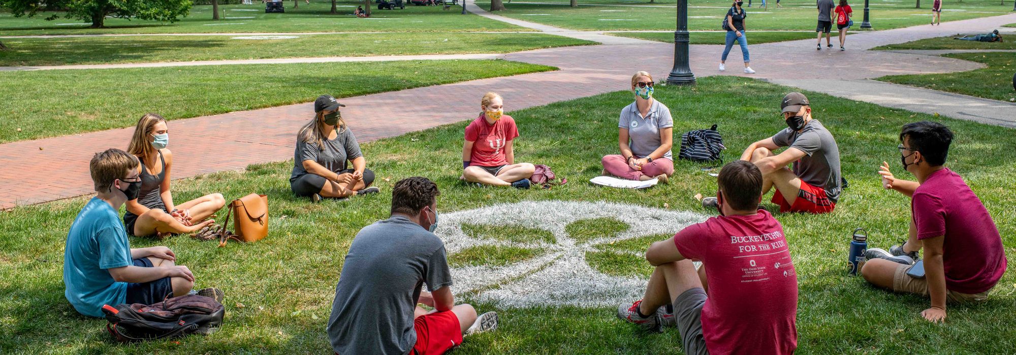 students sitting around a buckeye leaf painted on the oval to encourage social distancing
