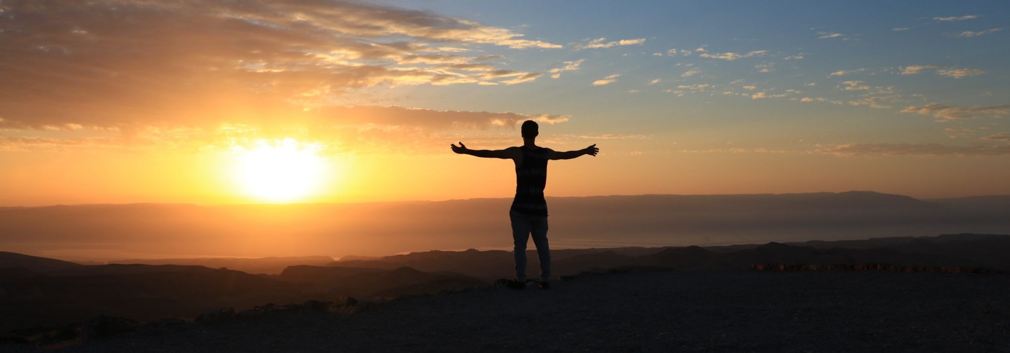 silhouette of man with arms outstretched in front of a sunset