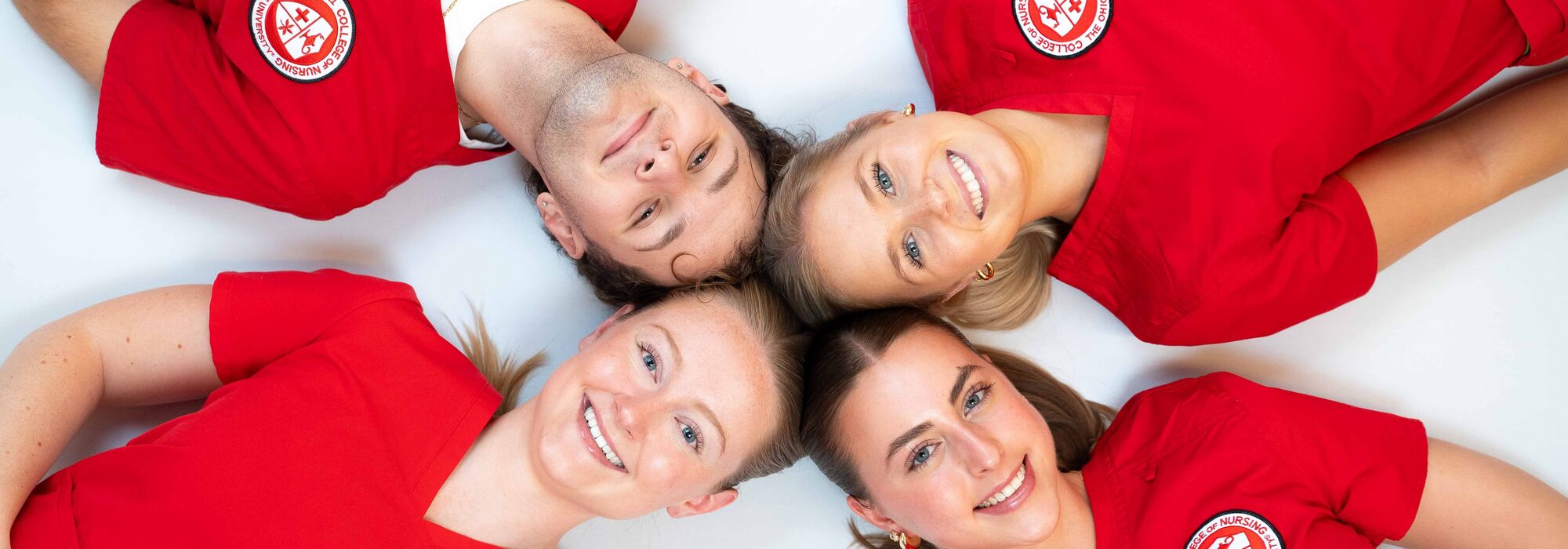 Four nursing students in red scrubs lying down with heads together