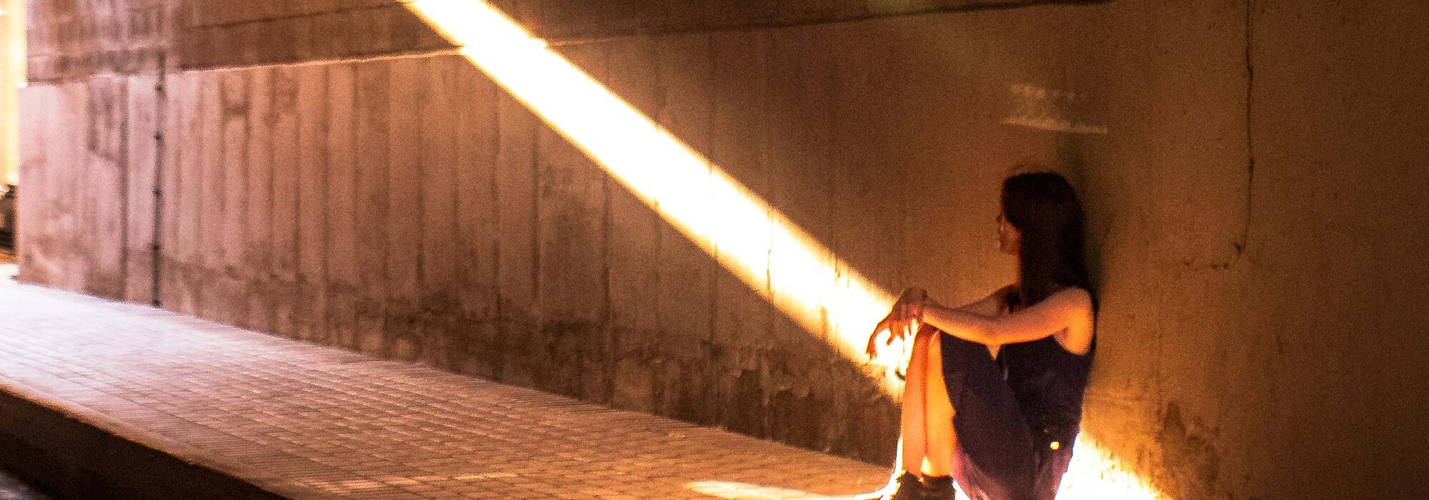 Adolescent girl sitting under overpass looking toward to the light