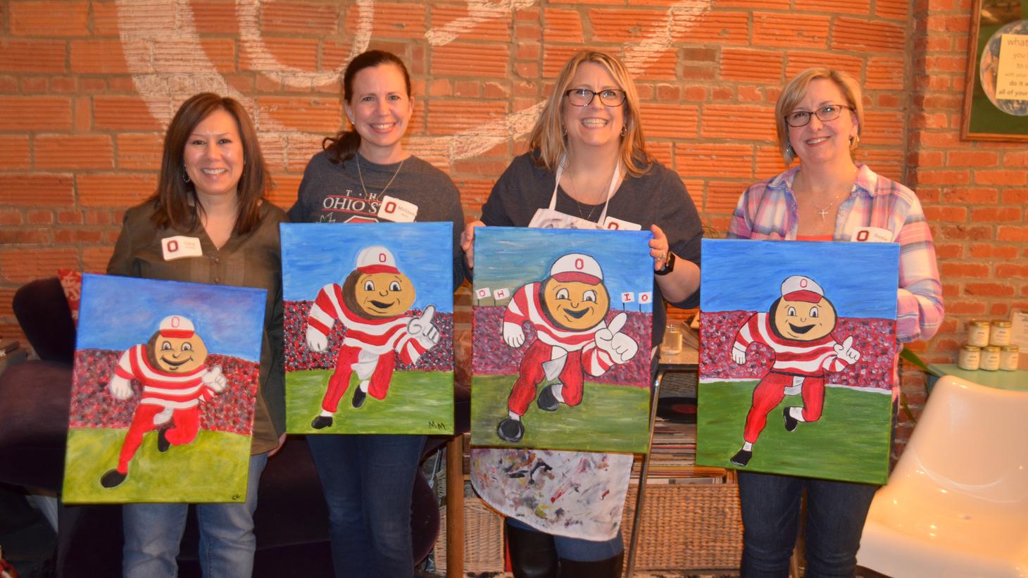 group of alumni pose with their paintings at a paint and pour event
