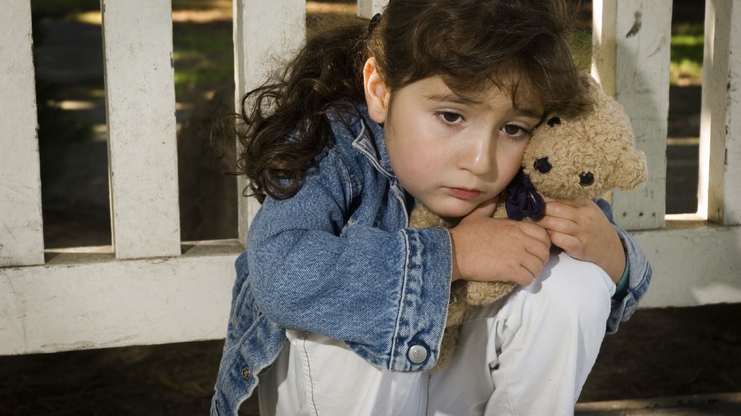 Young child holding a teddy bear and looking sad