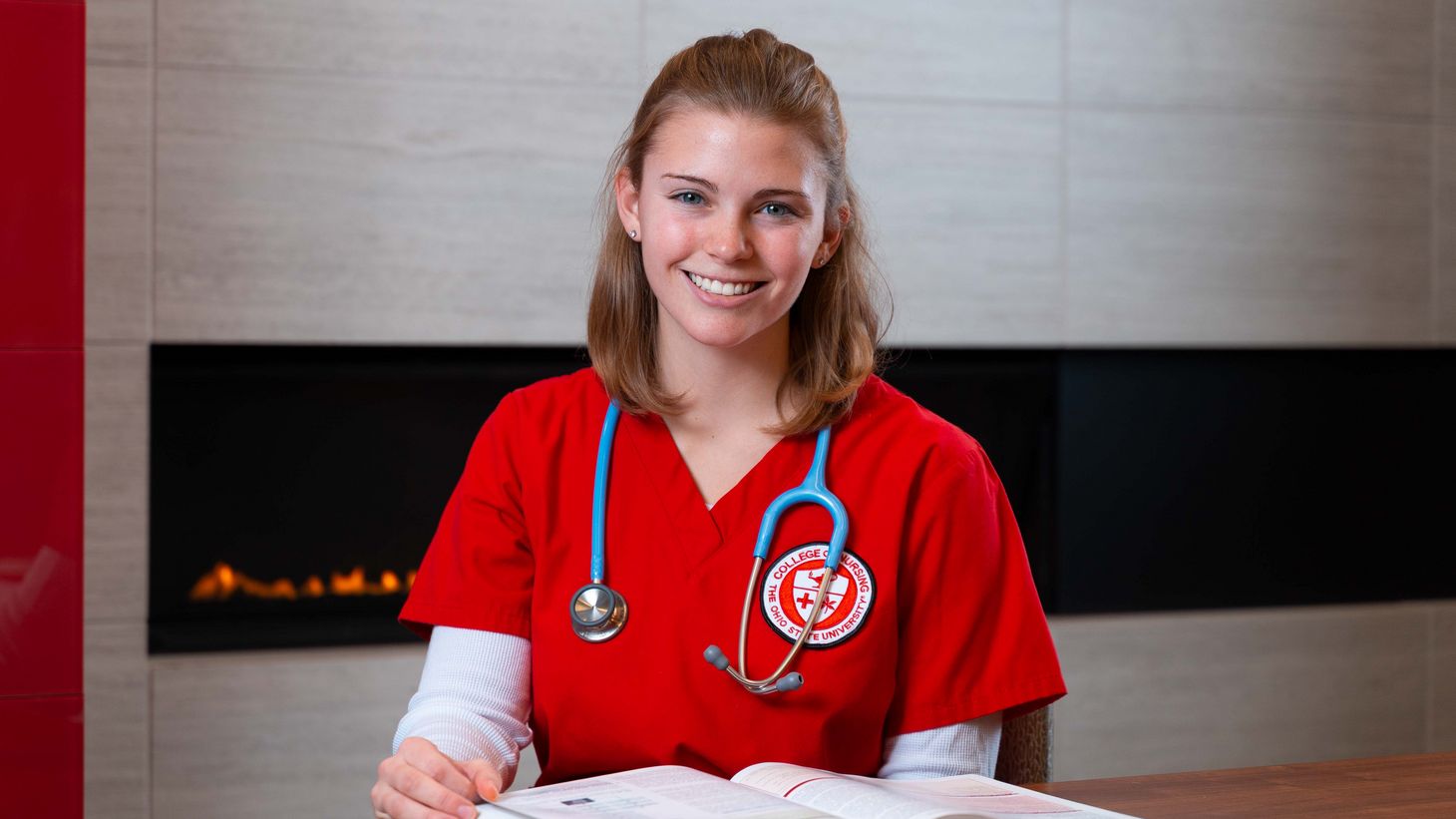 nursing student in red scrubs reading textbook