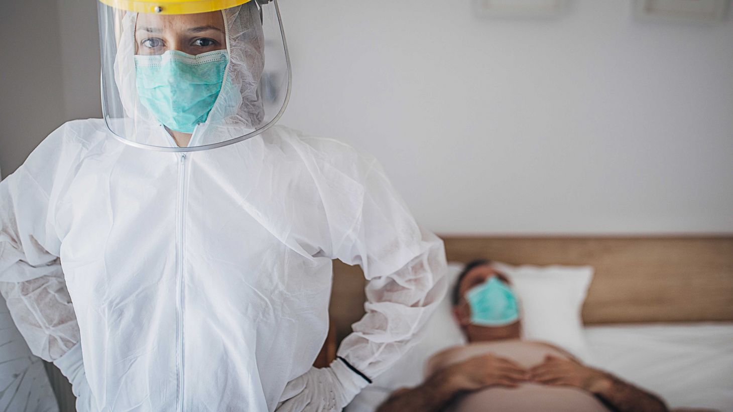 health care provider in personal protective equipment standing next to patient in bed wearing face mask