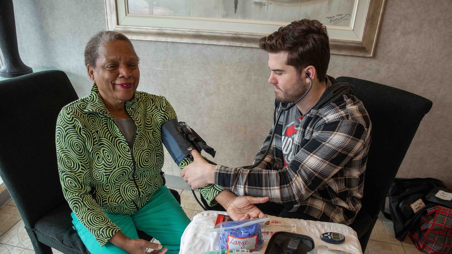 a white male nursing student checking the blood pressure of an older black woman