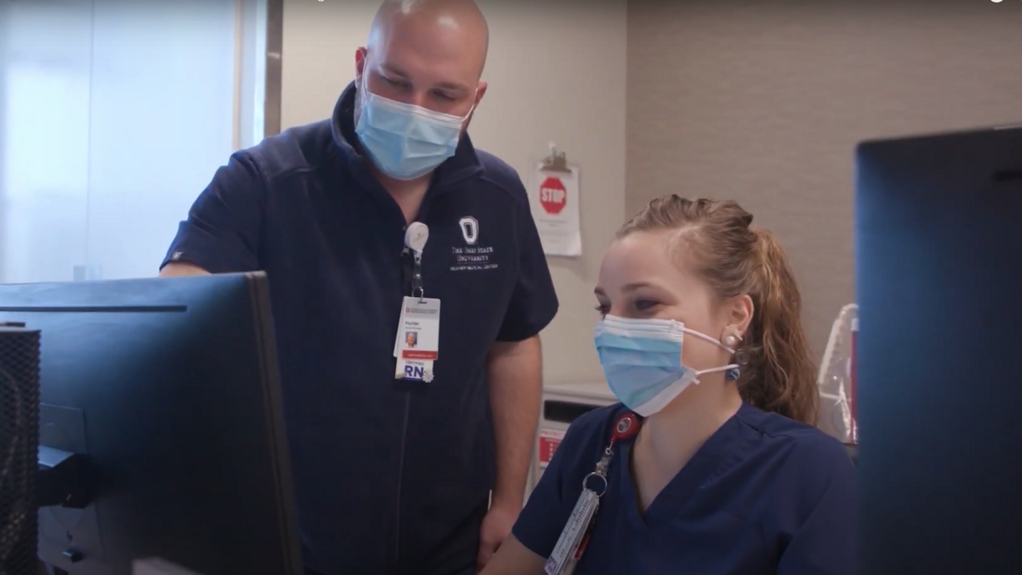 male and female nurse wearing face masks collaborating at computer