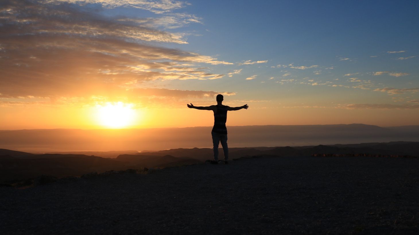 silhouette of man with arms outstretched in front of a sunset