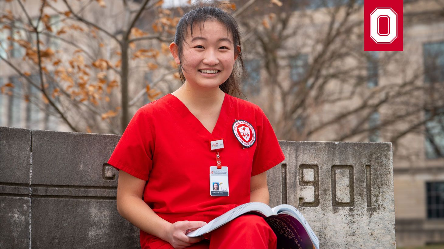 nursing student in red scrubs sitting on bench with textbook