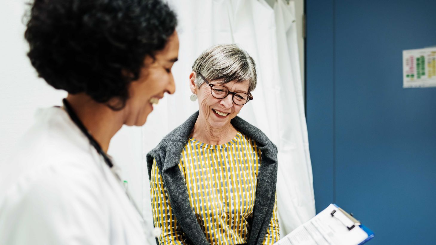 elderly woman speaking with healthcare provider holding a clipboard