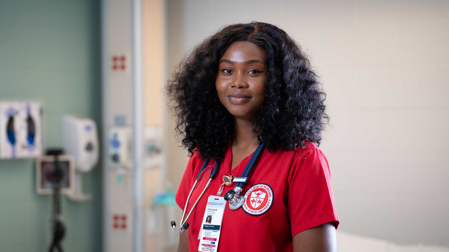 nursing student in red scrubs standing in simulation hospital room