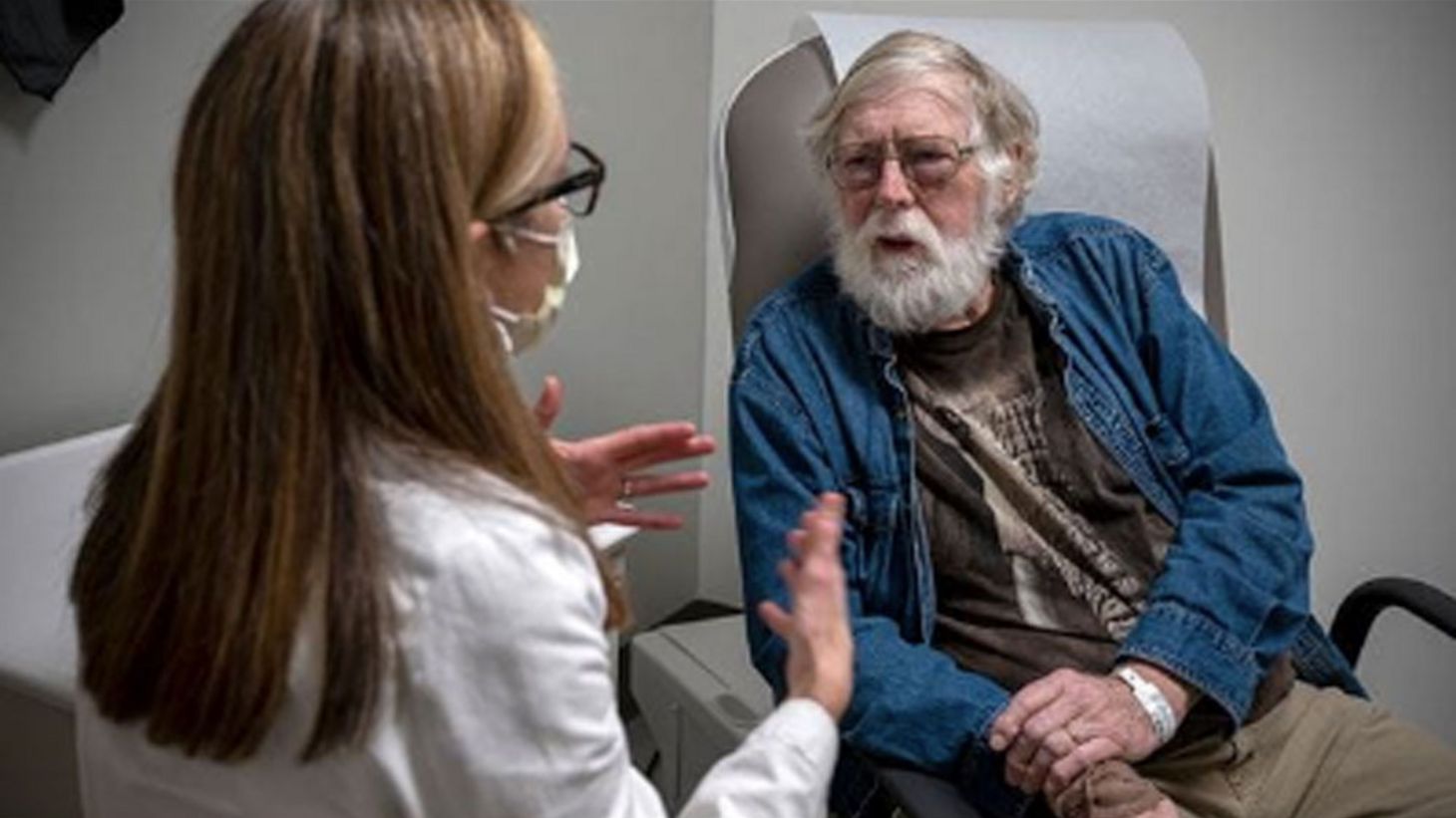 female researcher in white coat speaking with elderly male patient