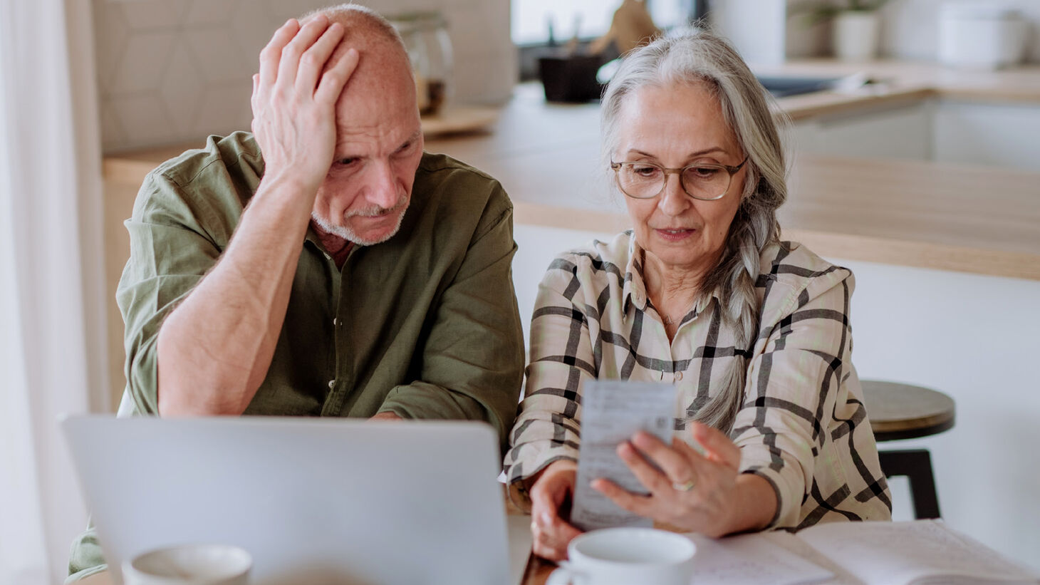 elderly couple appearing stressed over receipt and laptop