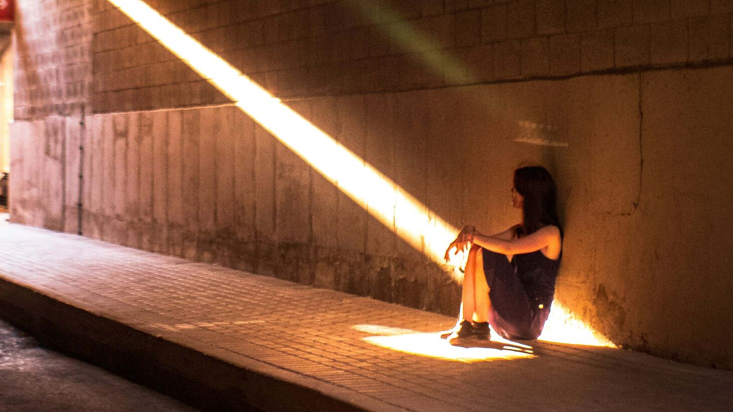 Adolescent girl sitting under overpass looking toward to the light