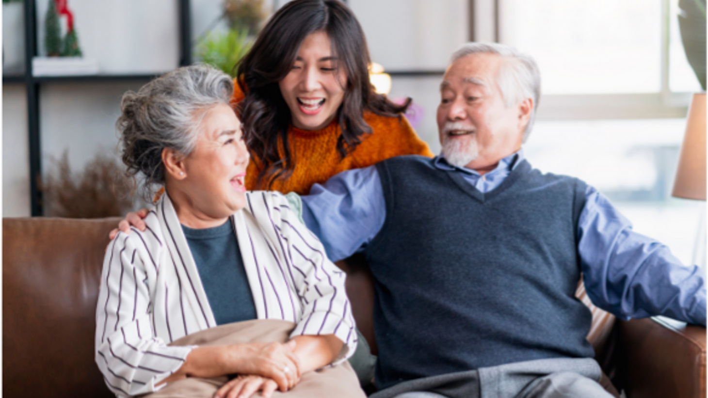 Senior Asian couple sitting on couch and young asian woman behind them, everyone smiling and happy 