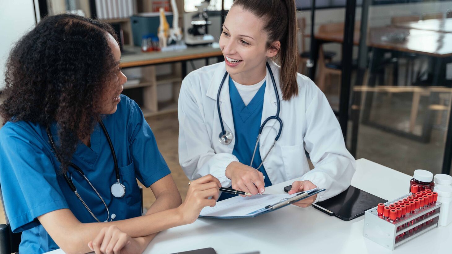 two women in a research lab talking about a document on a clipboard