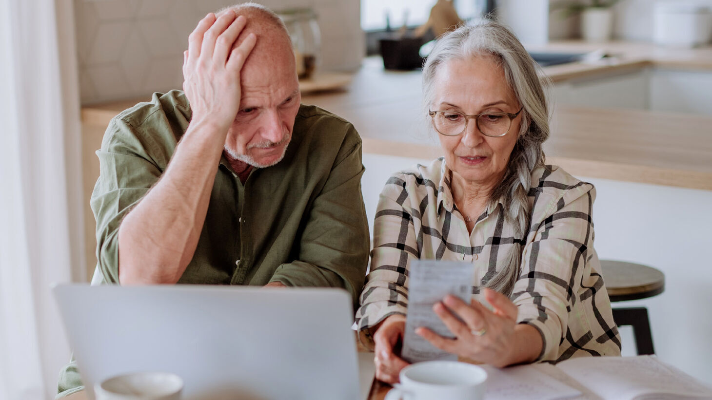 elderly couple appearing stressed over receipt and laptop