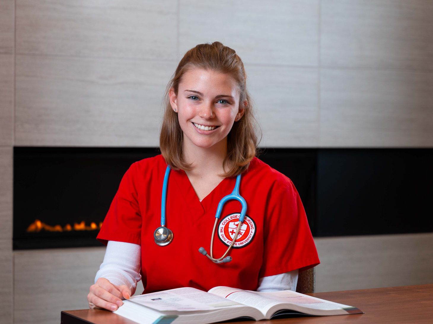 nursing student in red scrubs reading textbook