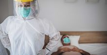 health care provider in personal protective equipment standing next to patient in bed wearing face mask
