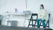 nurse in PPE sitting in a chair next to a table