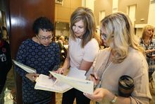 Three women at a conference looking at a sheet of paper in a binder.
