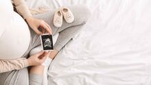 pregnant woman looking at ultrasound in her lap with a pair of baby shoes on her leg