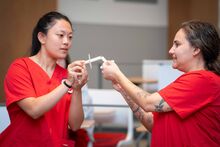 Two nursing students in red scrub light their candles