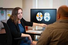 Michelle Failla points at brain scans on a computer screen while talking to a research subject