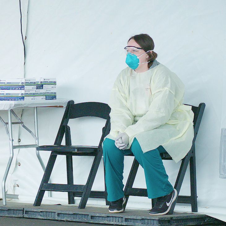 nurse in PPE sitting in a chair next to a table