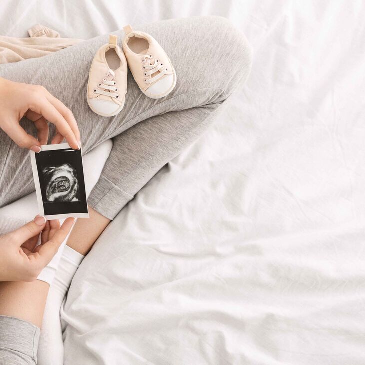 pregnant woman looking at ultrasound in her lap with a pair of baby shoes on her leg