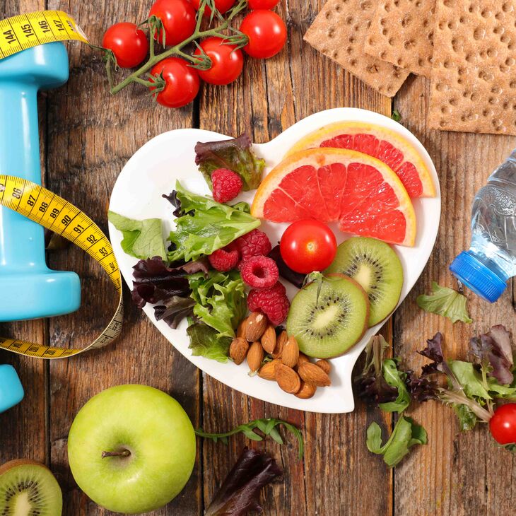 Elements of healthy lifestyle including fruits, vegetables, water, dumbbells, a tape measure