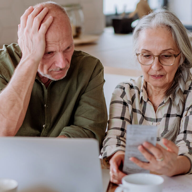 elderly couple appearing stressed over receipt and laptop