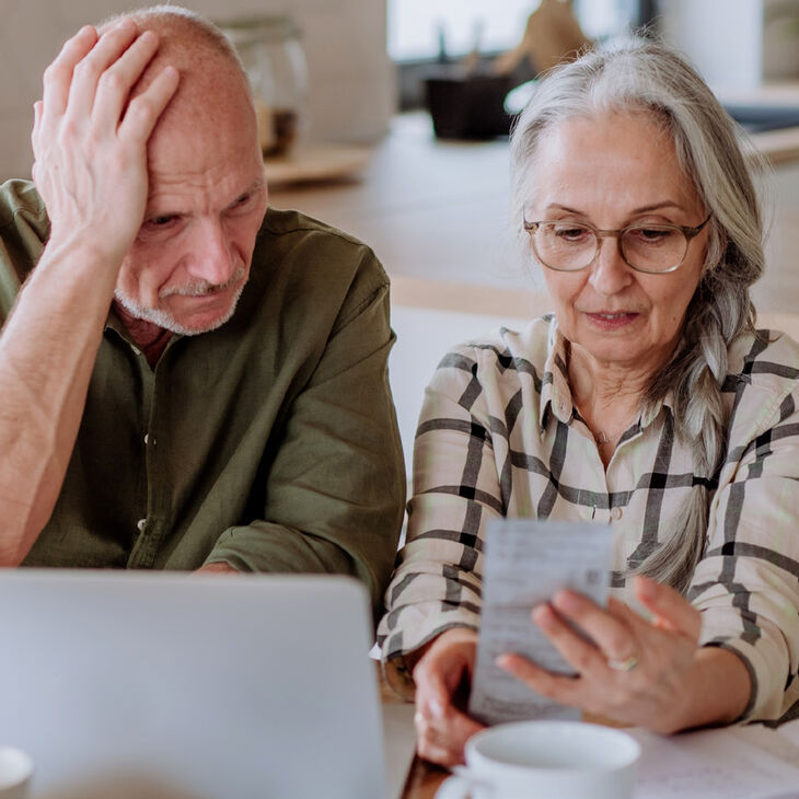 elderly couple appearing stressed over receipt and laptop