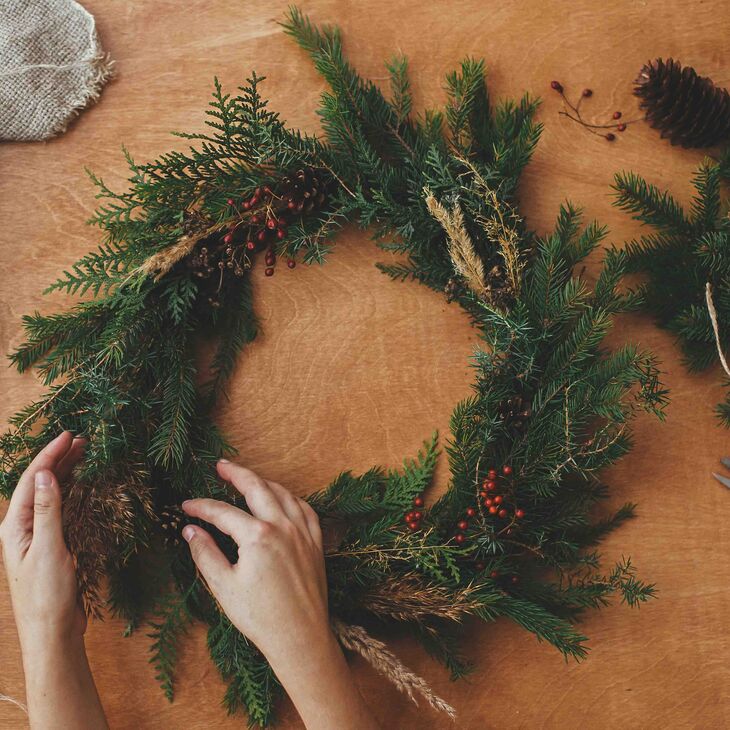 Hands working on a holiday wreath at a table with craft supplies