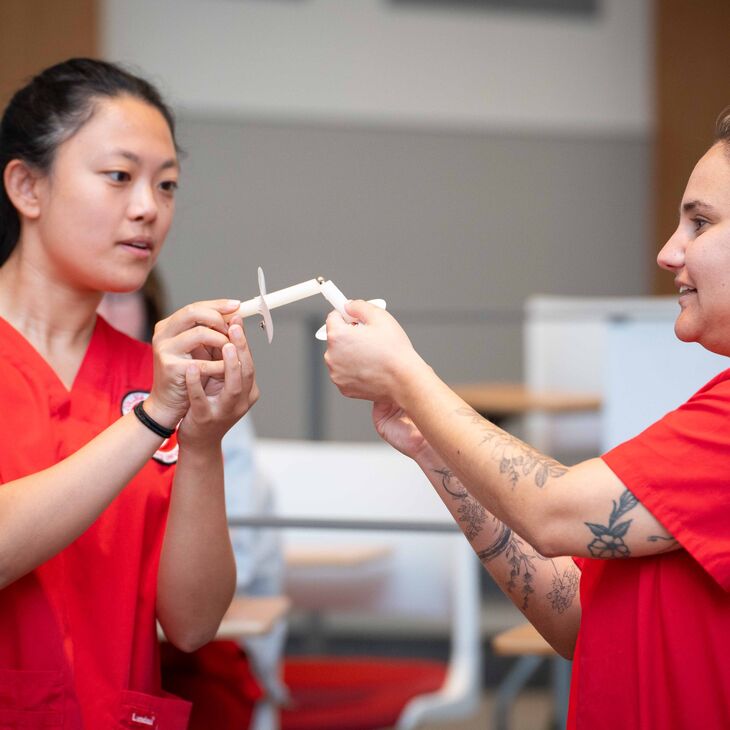 Two nursing students in red scrub light their candles