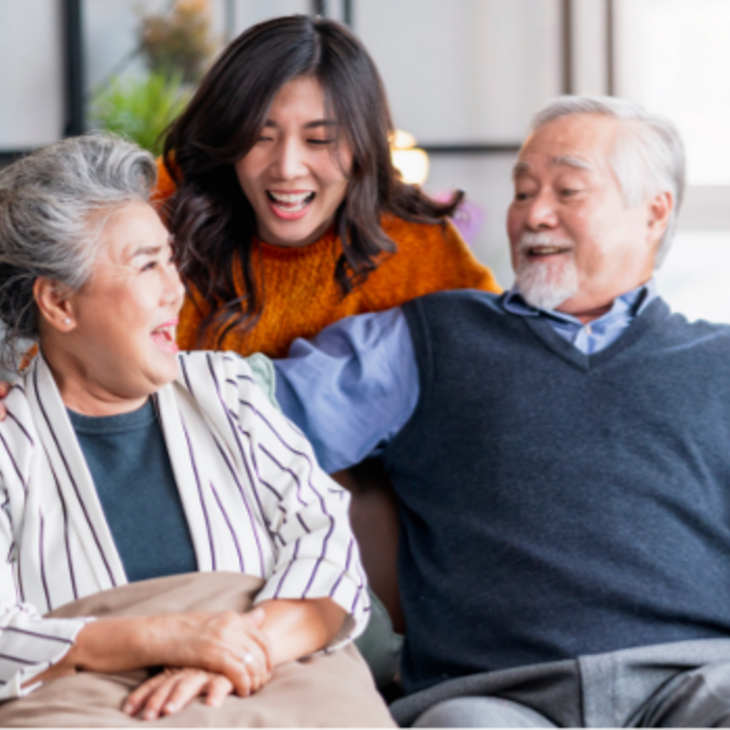 Senior Asian couple sitting on couch and young asian woman behind them, everyone smiling and happy 