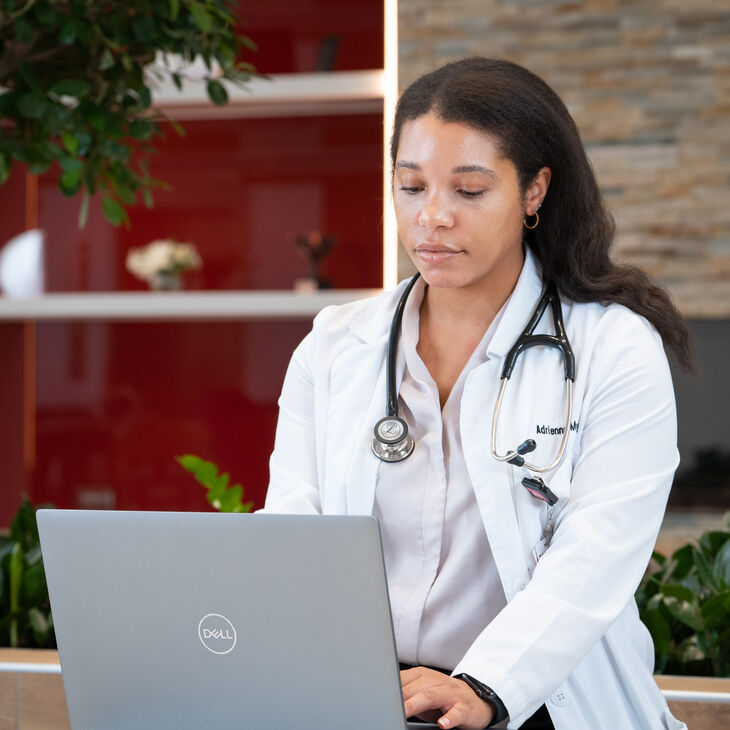 student in white lab coat sitting at computer